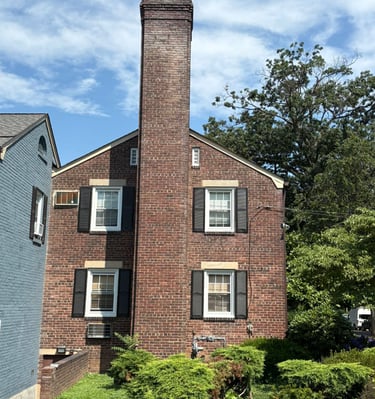 A tall, outdoor brick chimney on a house in Roslyn, New York, undergoing inspection for a major rebuild and repair project by