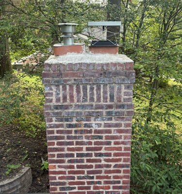 A brick chimney on a brown tiled roof with smoke rising from it, illustrating a safe and active fireplace system
