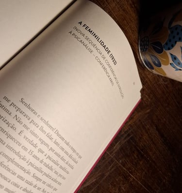 Página aberta do livro de Freud “Amor, Sexualidade, Feminilidade” em foco, com caneca ao lado, desta