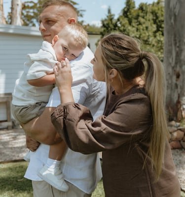 three people, one adult holding a child while another touches the child's nose