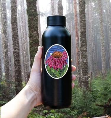 Hand holding a black reusable water bottle with a flower sticker in a foggy evergreen forest.
