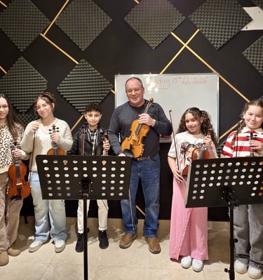 A smiling music teacher and his diverse group of violin students pose with their instruments in a sound-proofed studio.