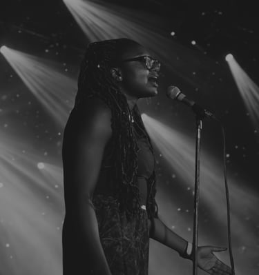 Iheoma Uzomba performing poetry with stage lights over head and open mic black and white