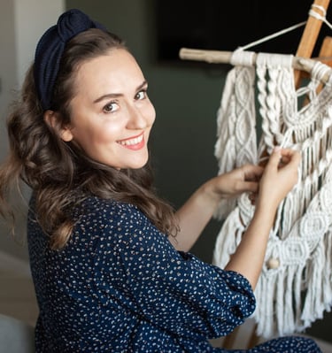 Una mujer sonriente creando un tapiz mural de macramé blanco hecho a mano.