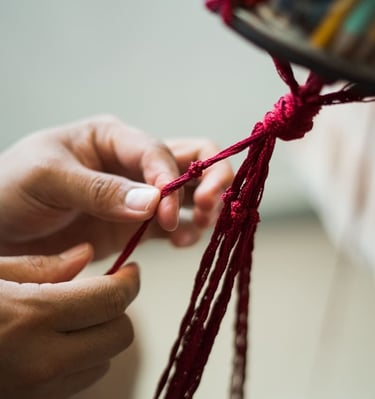 Mano atando un nudo decorativo con hilo rojo para un proyecto artesanal tradicional.