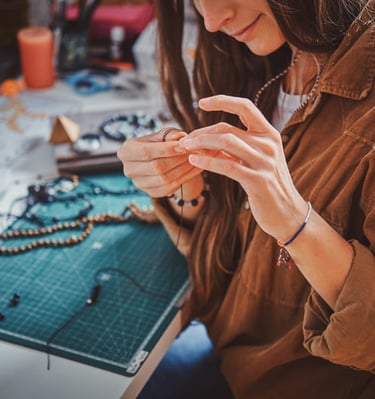 Un creador de joyería elaborando un collar de cuentas hecho a mano en una mesa de trabajo.