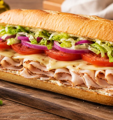 Fresh turkey sub sandwich on a baguette with melted cheese, tomatoes, onions, and lettuce.
