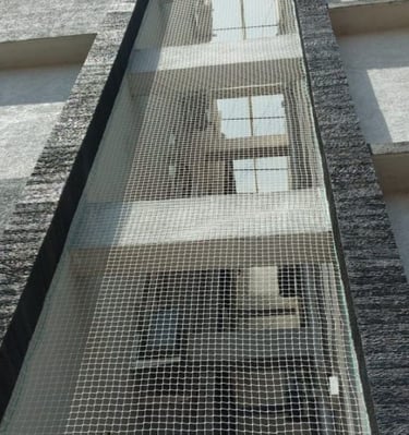 Evening view of a balcony fully protected by pigeon netting, with city lights in the background.