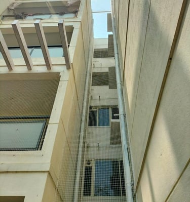 Wide shot of an apartment window covered with fine mesh pigeon netting in Sarjapur.