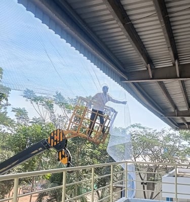 Technician carefully fixing pigeon netting along the warehouse roof edge.