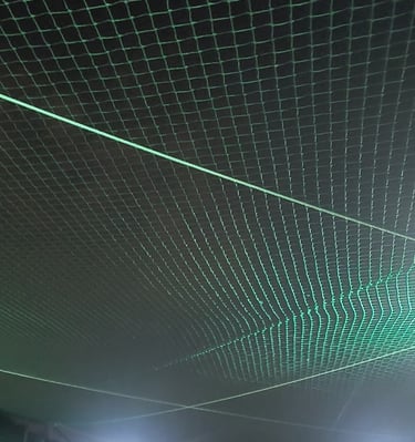 Technician from Arjilli Enterprises securing a sports net post under bright sunlight.