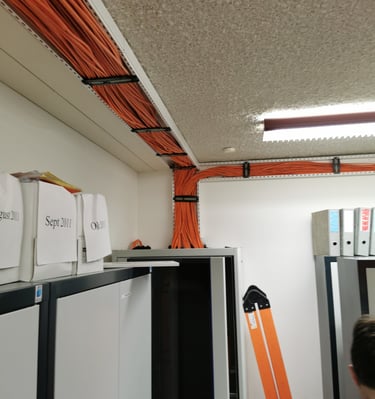 Organized orange ethernet cables managed in ceiling cable trays and server racks.