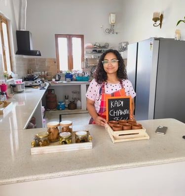 A smiling chef in a modern kitchen presenting Kadhi Chawal in traditional clay pots on a wooden tray.