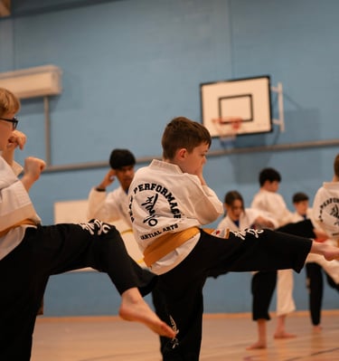 Young children practicing karate side kicks in a martial arts class wearing white uniforms and colored belts.