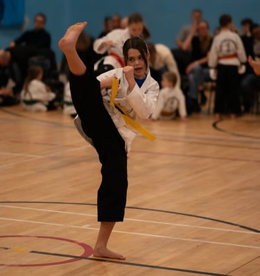 Young martial artist performing a high side kick during a karate competition in a gymnasium.