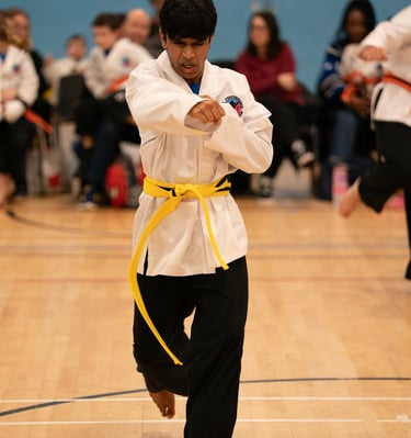 A young martial artist in a white uniform and yellow belt performs a karate punch at a competition.