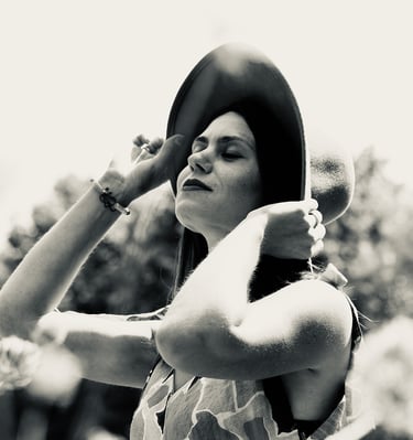 Photo en noir et blanc d'une jeune femme qui lève la tête et qui retient avec ses mains son chapeau