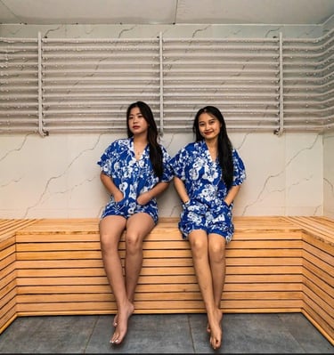 two women in matching blue pajamass sitting on a sauna bench