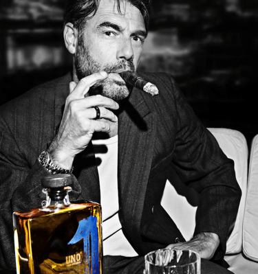 a man smoking a cigar with a bottle of uno tequila añejo