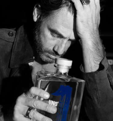 a man with a beard, holding a bottle of uno tequila blanco