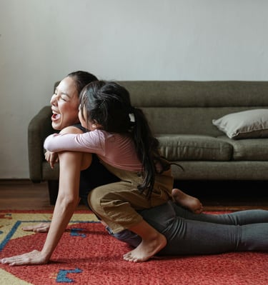 A mother in updog yoga pose. Her toddler is giving her a hug and kissing her.