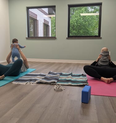 Two mothers laying on two yoga mats. Both are holding their infants.