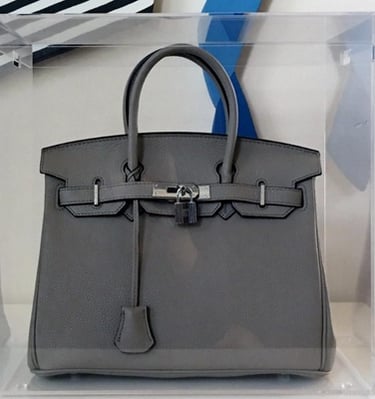 Clear acrylic display case with a grey handbag inside.