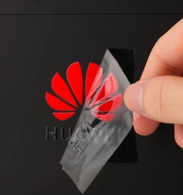 Clear UV DTF transfer sticker being peeled off a red Huawei logo.