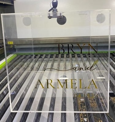 Clear acrylic wedding box with 'Bryn and Armela 04.08.24' in gold and black lettering.