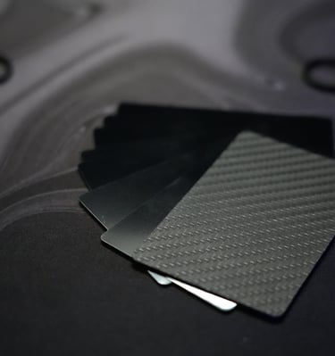 A stack of premium carbon fiber credit cards and metal wallet cards on a dark marble surface.