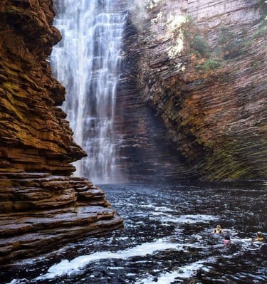a person swimming in a river near a waterfall