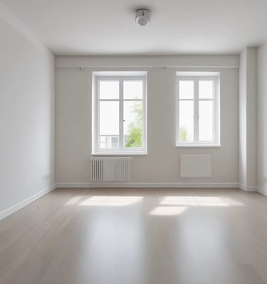 A construction vehicle with a hydraulic arm is actively engaged in demolishing a section of a house. The exterior wall of the house is partially torn down, exposing the framework and interior. Debris, including pieces of wood and siding, is scattered across the ground. The surrounding area is wooded, with trees visible in the background.