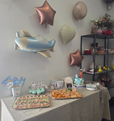 Baby shower catering table with an airplane balloon, blue cupcakes, and finger food platters.