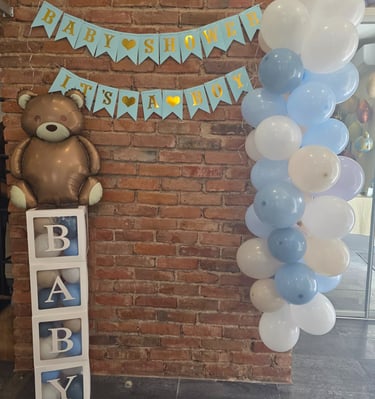 Baby shower decorations for a boy featuring a teddy bear balloon and blue balloon arch.