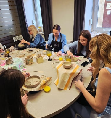 People participating in a handmade pottery workshop, sculpting and painting clay bowls at a studio table.