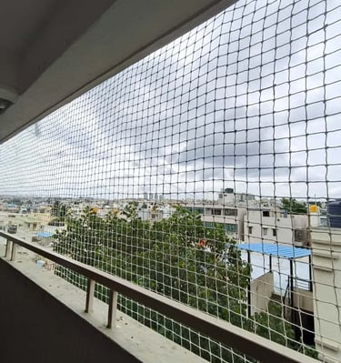 Wide shot of a KR Puram apartment balcony fully covered with pet safety nets, sunlight casting shado