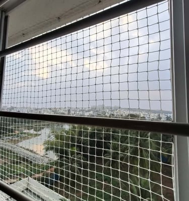 Technician carefully fixing pigeon net on a window frame in a high-rise apartment.