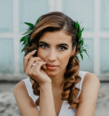 Portrait of a bride with curly hair and a green leaf headpiece in front of a blue door.