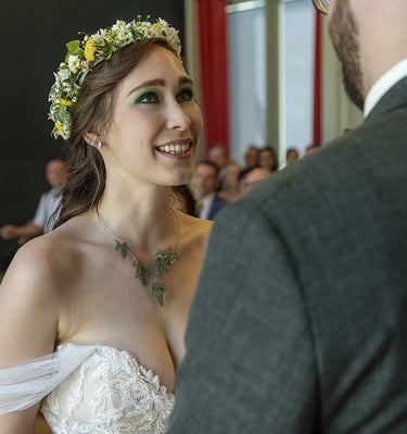 Ein Nahaufnahme-Foto einer lächelnden Braut, die nach oben zu ihrem Bräutigam blickt, dessen Rücken teilweise im Vordergrund 