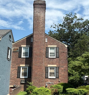 A tall, outdoor brick chimney on a house in Roslyn, New York, undergoing inspection for a major rebuild and repair project by