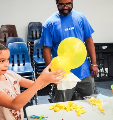 a young girl holding a yellow balloon in a classroom as part of her space capsule landing system