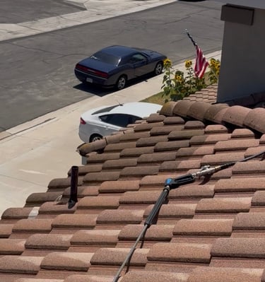 A pressure washing wand sits on a clay tile roof during a residential exterior cleaning service.