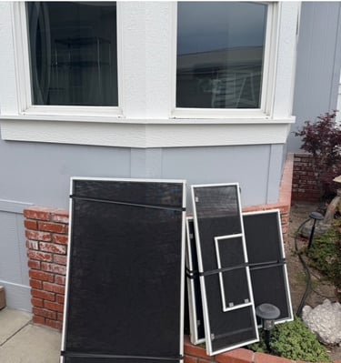 Replacement window screens leaning against a mobile home exterior with brick accents.