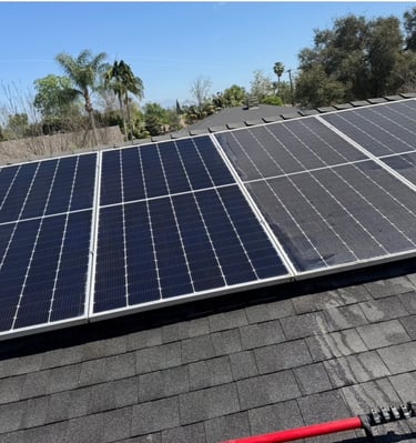 Residential solar panel installation on a dark shingle roof with a clear blue sky background.