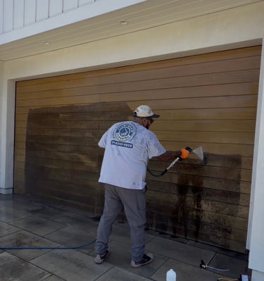 A professional technician power washing a wooden garage door to remove dirt and stains.