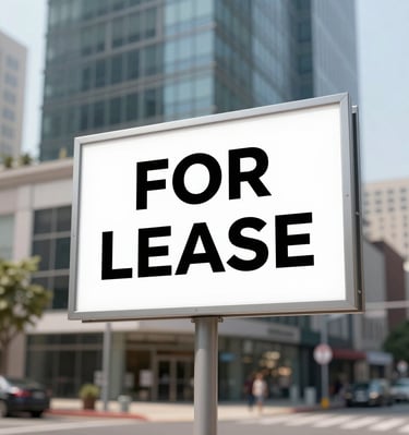 A white 'For Lease' sign stands in front of a modern commercial office building in a city.