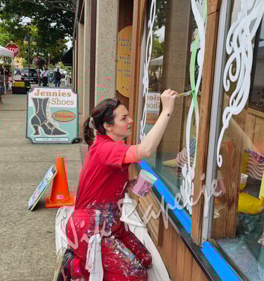 woman painting an artistic design on a shop window