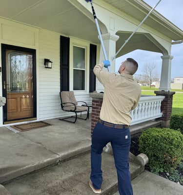 Pest control technician removing spider webs from house