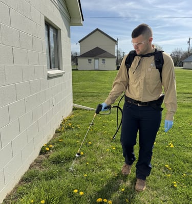 Pest control technician spraying around foundation of garage
