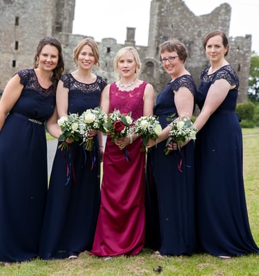 Bride with bridemaids, all stood in a row with boquets all held together. Castle in the beeeeeee